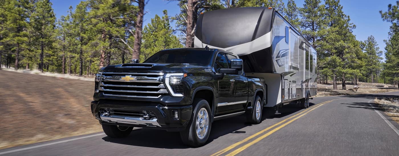 Black 2026 Chevy Silverado 2500 towing a camper down a road
