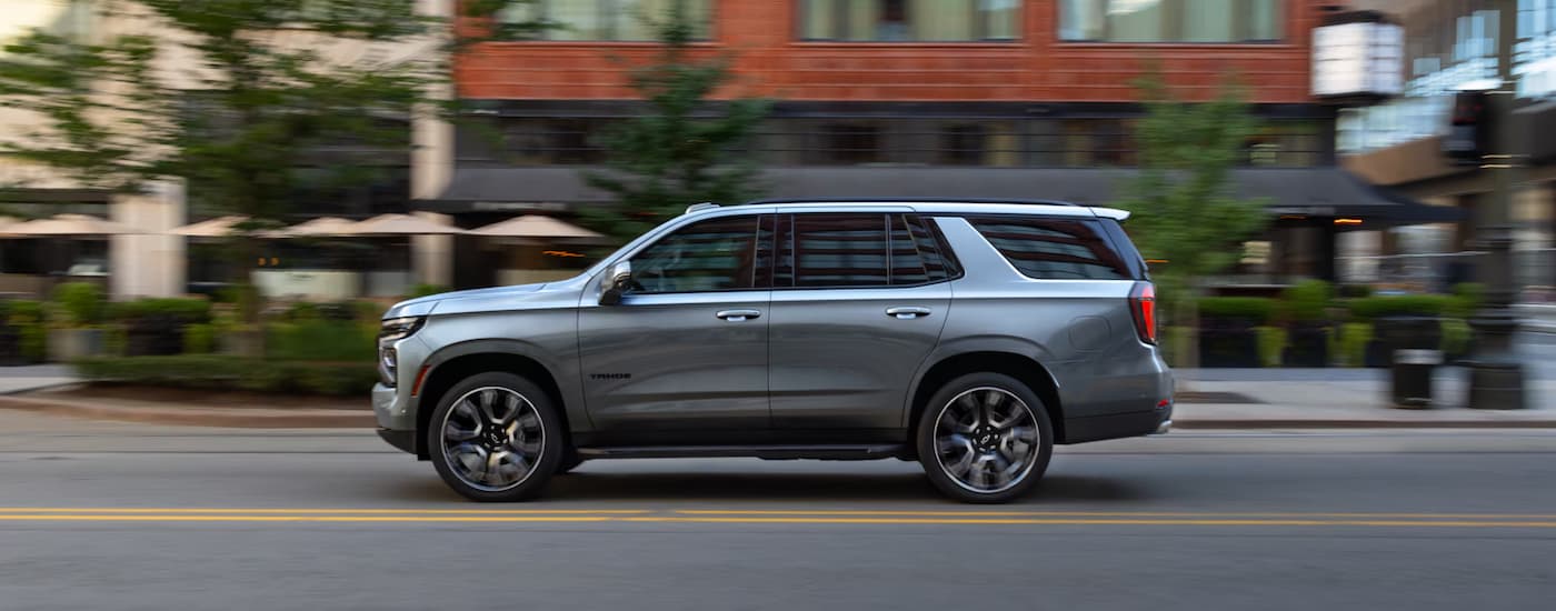 Side of a grey 2026 Chevy Tahoe driving down a city street.