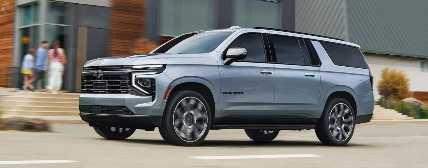 Grey 2026 Chevy Suburban driving past an apartment building.
