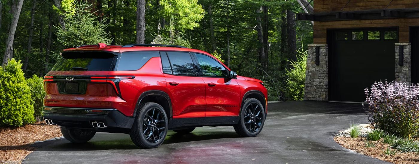 A rear-facing red 2026 Chevy Traverse parked in front of a garage.